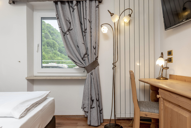 Helles Schlafzimmer mit Fenster, Vorhang, Schreibtisch und Stehlampe.