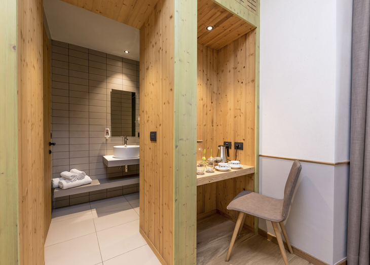 Moderner Innenraum mit Holzwänden, Stuhl, Tisch und Badezimmer im Hintergrund.