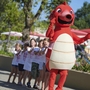 Kinder stehen lachend in einer Reihe hinter einem roten Maskottchen im Park Umag.