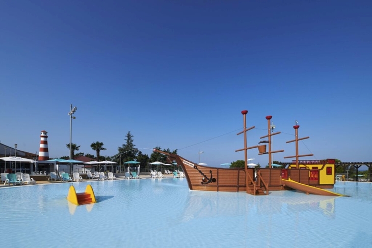 Großes Schwimmbecken mit Piratenschiff-Spielplatz und Leuchtturm im Hintergrund.