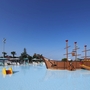 Großes Schwimmbecken mit Piratenschiff-Spielplatz und Leuchtturm im Hintergrund.