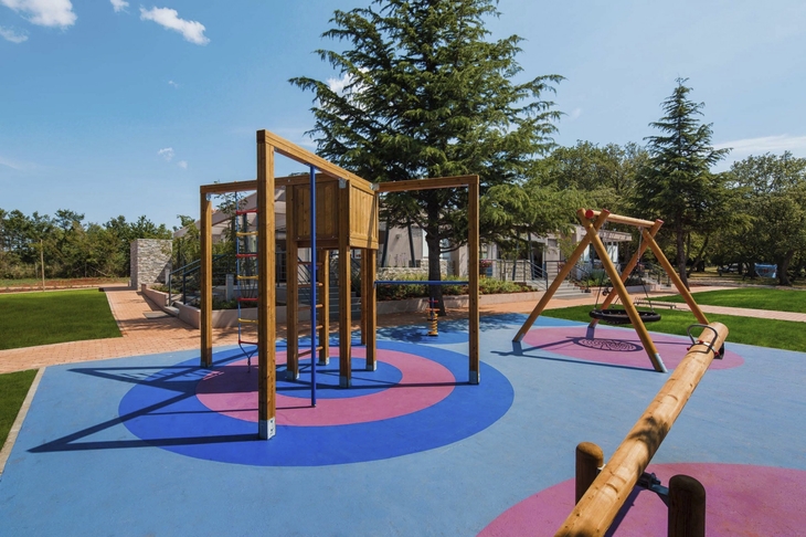 Spielplatz im Freien mit Klettergerüst und Rutsche auf buntem Boden.