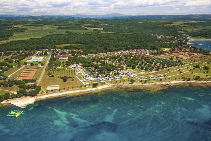 Luftaufnahme eines Campingplatzes am Meer mit grüner Umgebung und klarem Wasser.