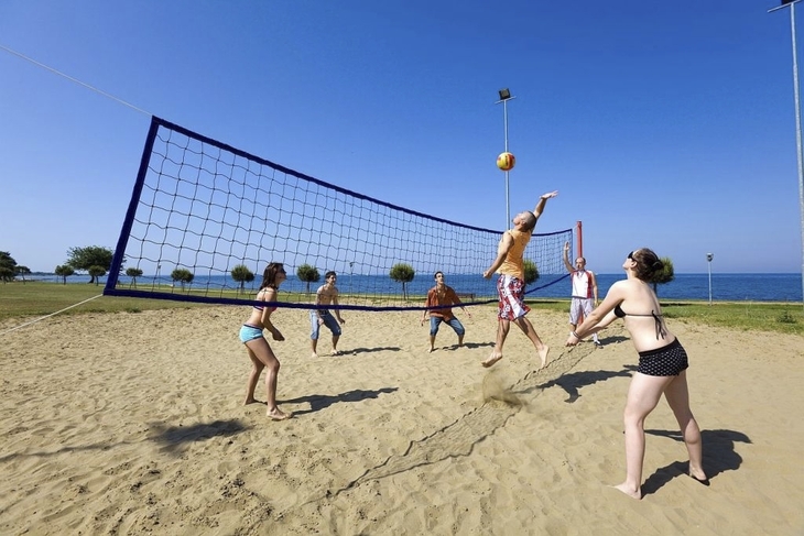 Personen spielen Volleyball im Sand, mit Meer im Hintergrund.