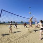 Personen spielen Volleyball im Sand, mit Meer im Hintergrund.