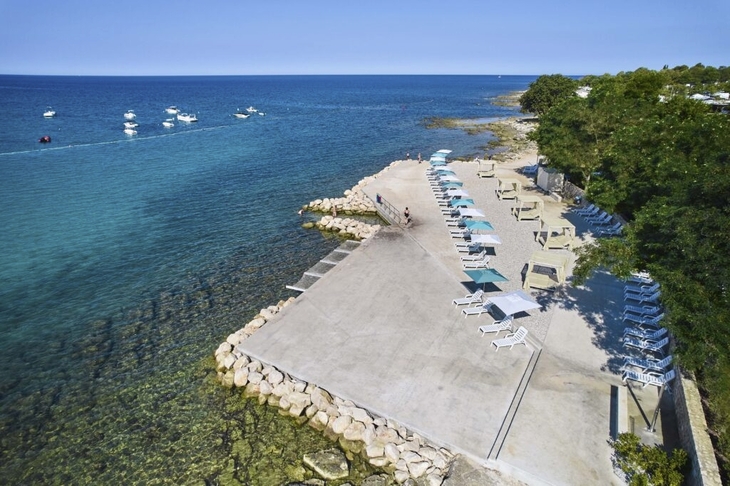 Strandpromenade mit Liegen und Sonnenschirmen am blauen Meer in Umag, Kroatien.