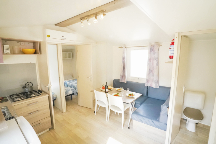 Innenansicht eines Mobilheims mit Tisch, Stühlen, Sofa und Küche.