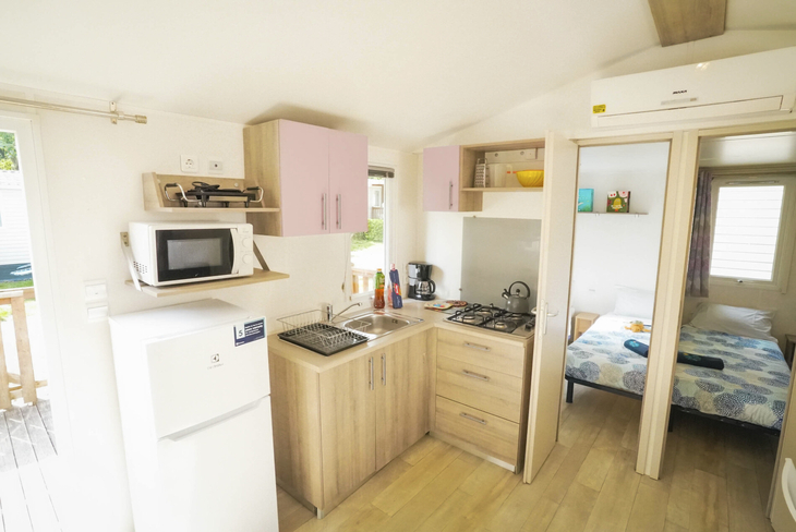 Küche und Schlafzimmer in einem Mobilheim mit Holzoptik.