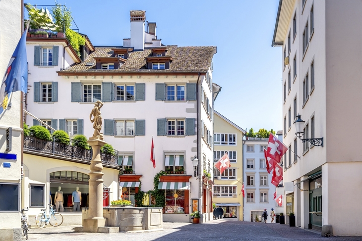 Straße in der Altstadt von Zürich mit historischen Gebäuden und Schweizer Fahnen.