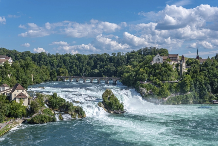 Rheinfall in Neuhausen mit Schloss und Brücke im Hintergrund bei klarem Himmel.