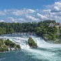 Rheinfall in Neuhausen mit Schloss und Brücke im Hintergrund bei klarem Himmel.