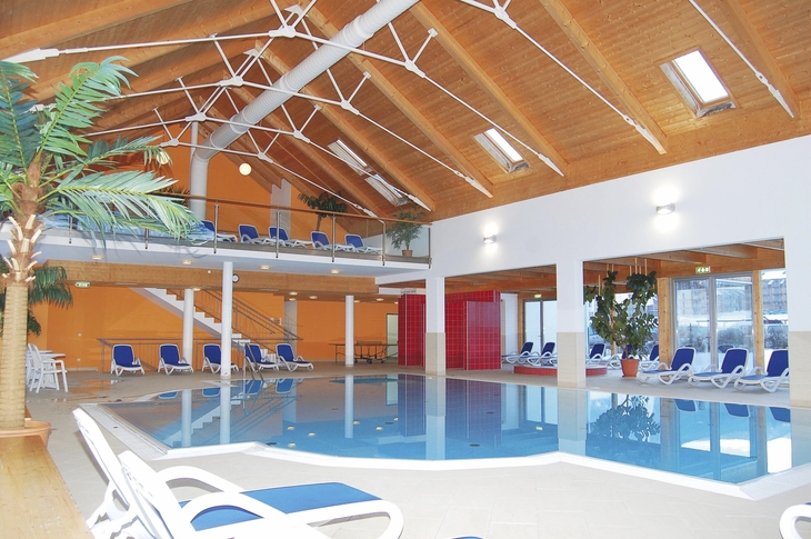 Innenbereich eines Hallenbades mit Liegestühlen und Holzdecke.