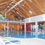 Innenbereich eines Hallenbades mit Liegestühlen und Holzdecke.