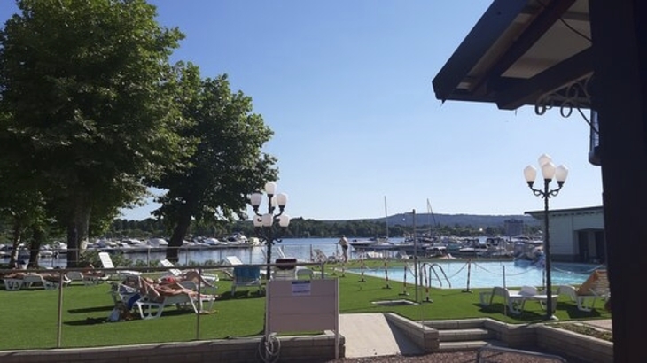 Sonnenliegen am Pool mit Blick auf einen See, Boote und Bäume im Hintergrund.