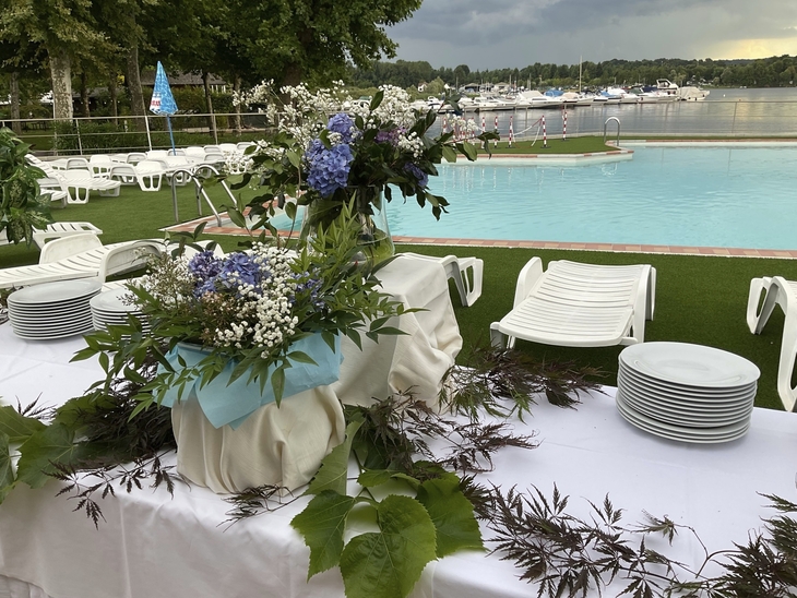 Gedeckter Tisch mit Blumenarrangement neben Pool, im Hintergrund Yachthafen.