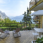 Terrasse mit Seeblick, zwei Liegestühlen, Tisch und Sonnenschirm, umgeben von Bergen.
