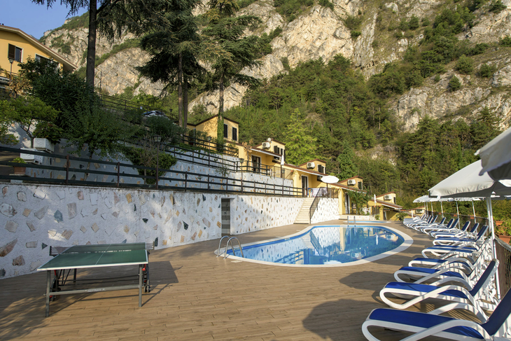 Sonnenterrasse mit Pool, Sonnenliegen und Tischtennisplatte vor Hügelkulisse.