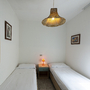 Zwei Einzelbetten in heller Wohnung mit Spiegel, Gemälden und Lampe.