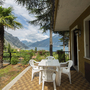 Terrasse mit Tisch und Stühlen, umgeben von Garten, Blick auf Berge und See.
