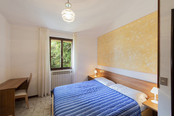 Schlafzimmer mit Doppelbett, Holzschreibtisch und Fenster mit Blick auf grüne Bäume.