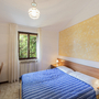 Schlafzimmer mit Doppelbett, Holzschreibtisch und Fenster mit Blick auf grüne Bäume.