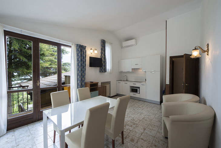 Helles Wohnzimmer mit Tisch, Stühlen, Küchenzeile und Zugang zu einem Balkon.