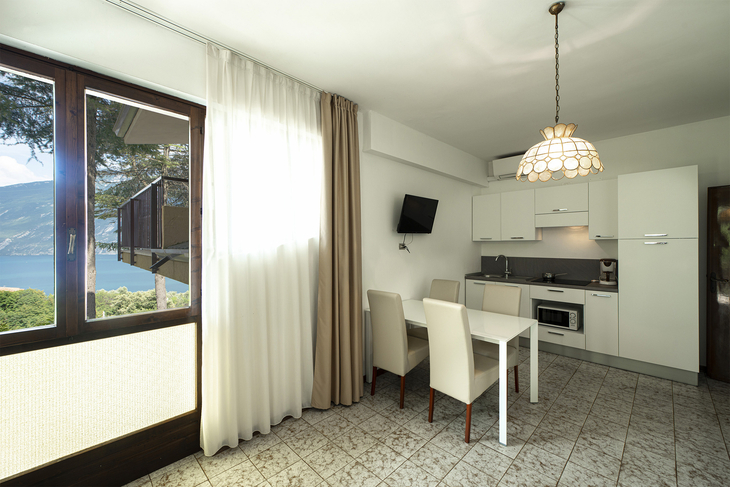 Helles Apartment mit Küchenzeile, Esstisch und Blick auf den See durch das Fenster.