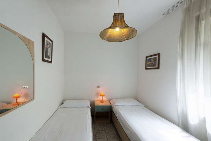 Zwei Einzelbetten in heller Wohnung mit Spiegel, Gemälden und Lampe.