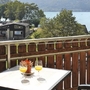 Blick von Balkon auf See und Hügel, zwei Gläser mit Getränken auf Tisch.