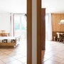 Zwei Räume mit Holzmöbeln und großen Fenstern; Schlafzimmer links, Wohnzimmer rechts.