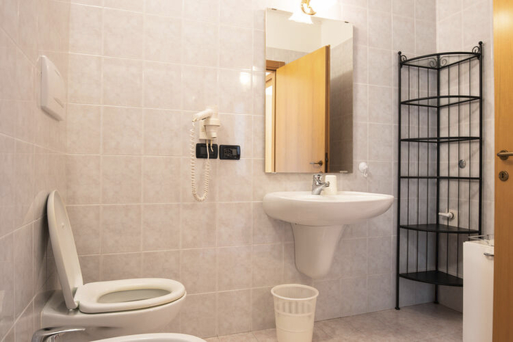 Badezimmer mit Waschbecken, Spiegel und Toilette in hellen Fliesen.