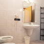 Badezimmer mit Waschbecken, Spiegel und Toilette in hellen Fliesen.
