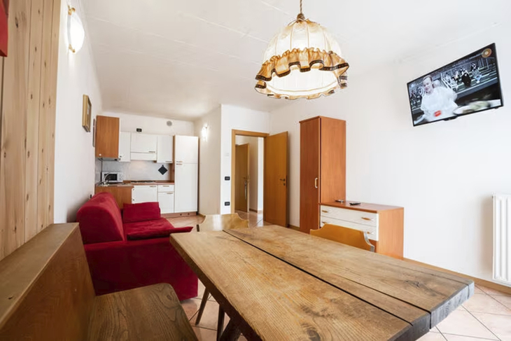 Essbereich mit Holztisch, rotem Sofa und Fernseher an der Wand.