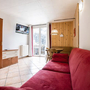 Wohnzimmer mit rotem Sofa, Esstisch, TV, großen Fenstern und Holzwand.