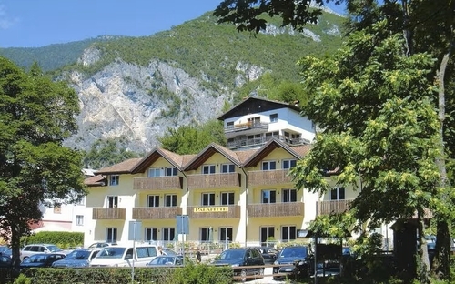 Gebäude im Alpenstil vor bewaldeten Bergen an einem sonnigen Tag.