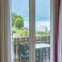 Blick durch ein Fenster auf einen Balkon mit See- und Berglandschaft im Hintergrund.