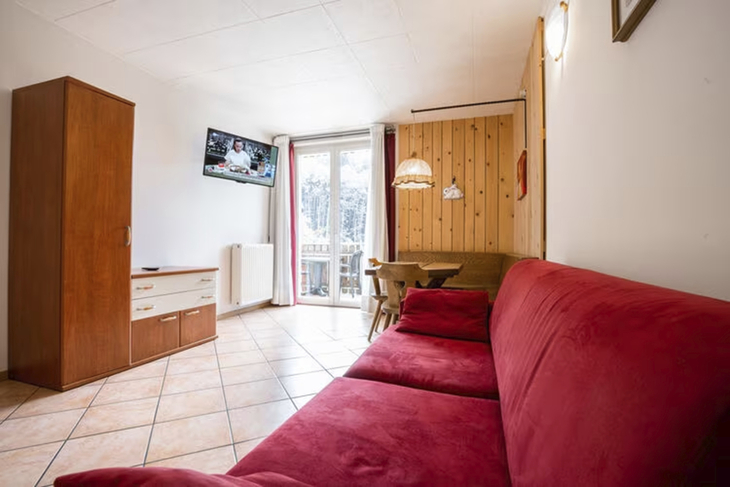 Wohnzimmer mit rotem Sofa, Esstisch, TV, großen Fenstern und Holzwand.