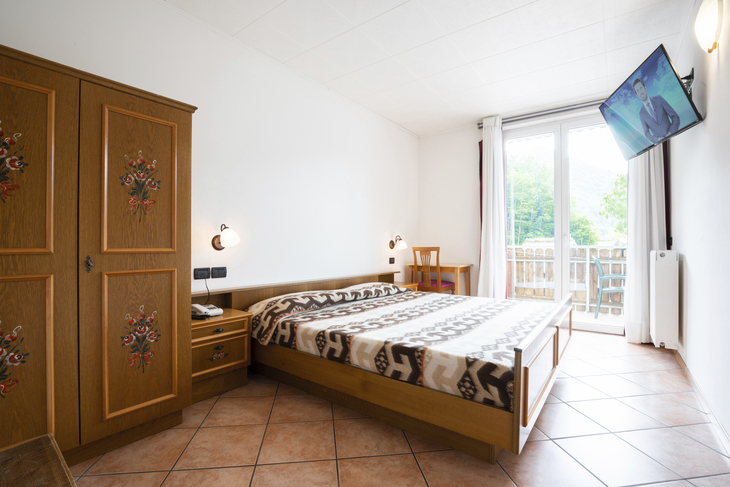 Helles Schlafzimmer mit Holzmöbeln, Doppelbett und Balkon mit Blick ins Grüne.