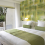 Helles Hotelzimmer mit Doppelbett und grünem Wanddesign, Blick auf Terrasse.