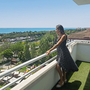 Frau auf Balkon mit Meerblick und grüner Landschaft im Hintergrund.