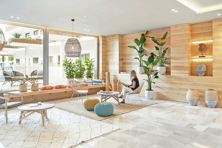 Moderne Hotel-Lobby mit Pflanzen, Sitzgelegenheiten und einer sitzenden Person.