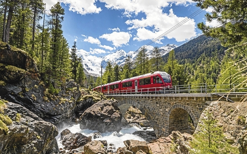Roter Zug der Bernina Bahn fährt über eine steinerne Brücke in bergiger Landschaft.