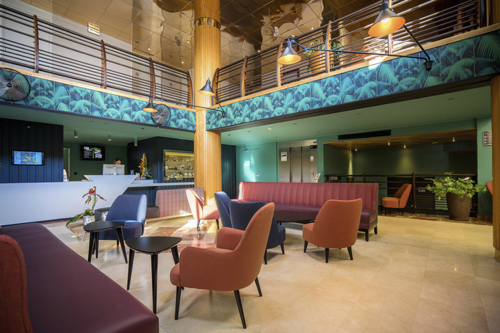 Modernes Hotel-Lobby mit bunten Sesseln, Empfangstresen und Pflanzen.