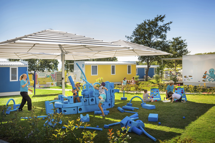 Spielplatz mit Kindern in einem Ferienresort, umgeben von kleinen Ferienhäusern.