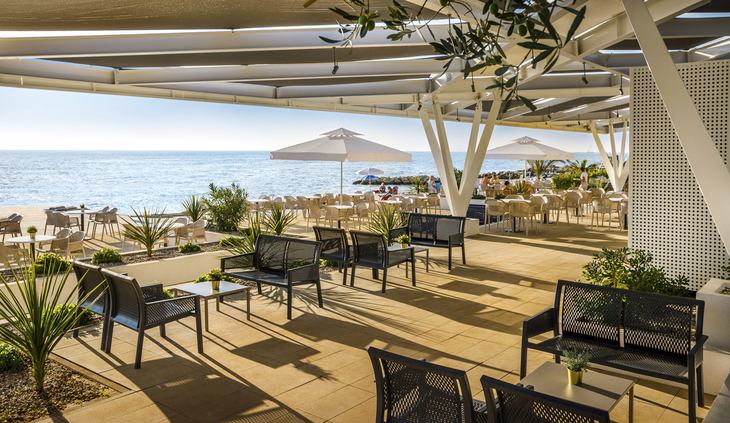 Terrasse mit Meerblick, Sitzbereich, Sonnenschirme und Pflanzen im Resort.