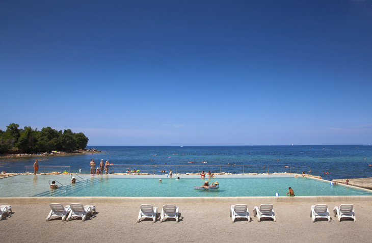 Infinity-Pool mit Menschen vor Meer in einem Resort bei klarem blauem Himmel.