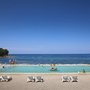 Infinity-Pool mit Menschen vor Meer in einem Resort bei klarem blauem Himmel.