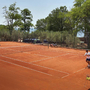 Tennisspiel auf einem Sandplatz mit zwei Spielern und Bäumen im Hintergrund.