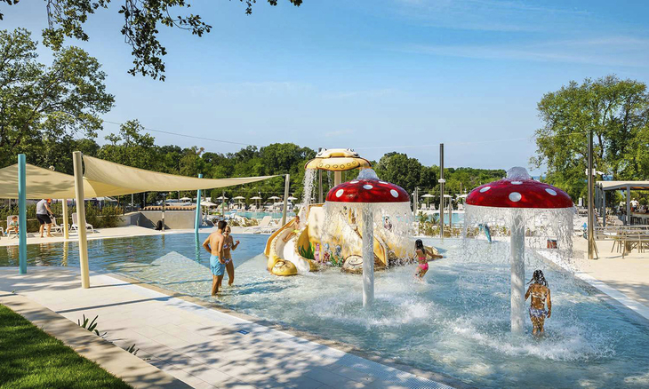 Kinder spielen in einem Poolbereich mit Wasserspielen und roten Pilzen.
