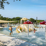Kinder spielen in einem Poolbereich mit Wasserspielen und roten Pilzen.